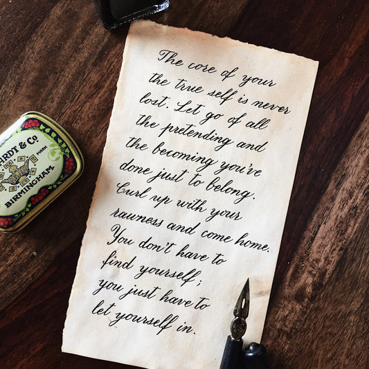 Vintage look calligraphy letter on a wooden surface, accompanied by a calligraphy pen and a nib storing tin